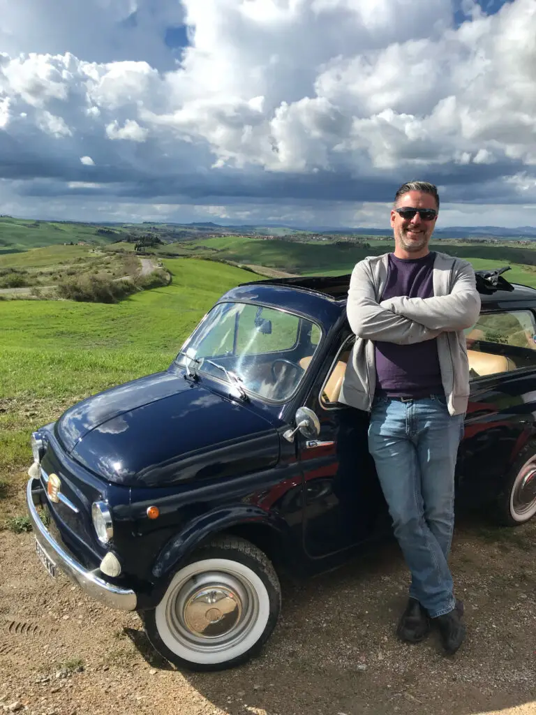 Dean Horvath, luxury travel advisor, standing beside a car in Tuscany.